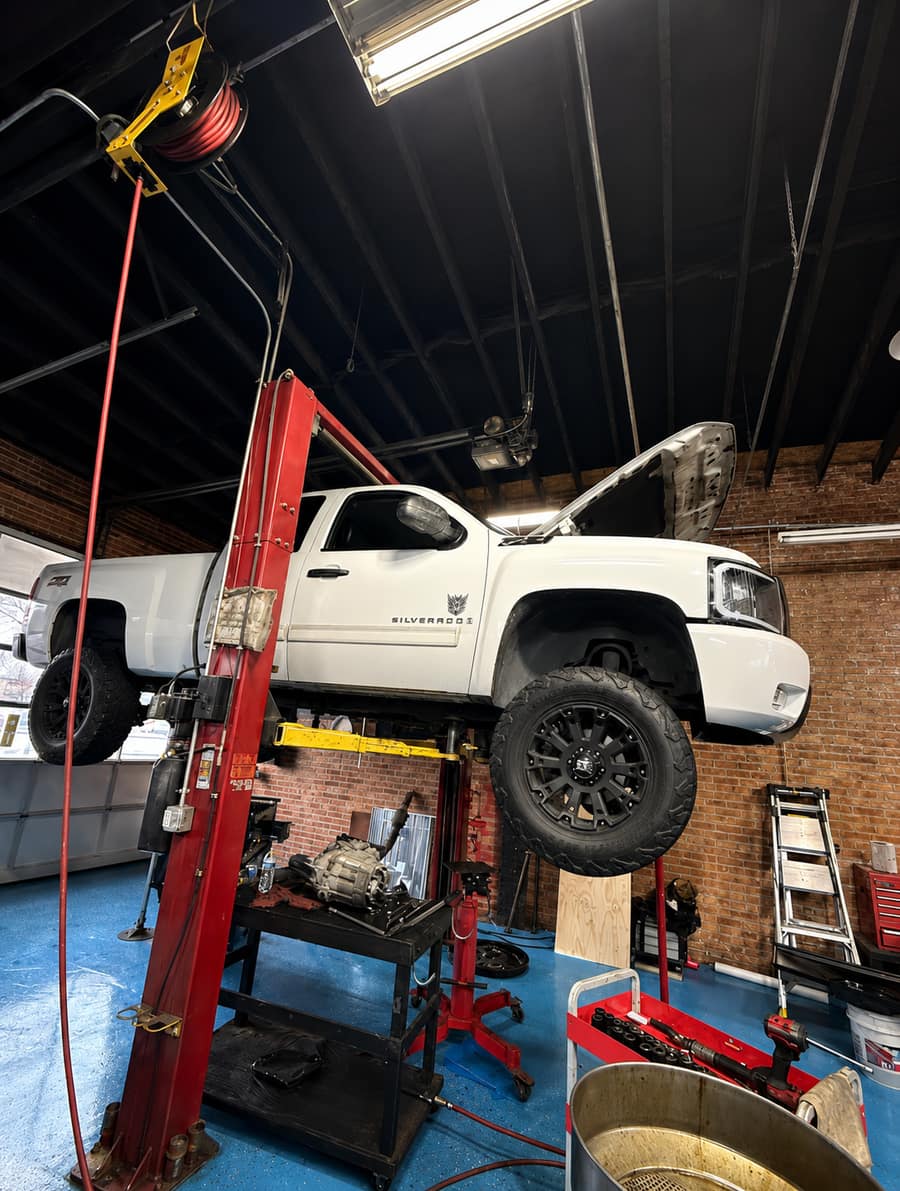 White Chevrolet Silverado raised on a vehicle lift inside the ERMAK Tires repair bay.